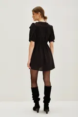 Vestido corto negro con mangas cortas con volados, escote con cuello redondo y abertura con lazos. Presenta cintura ajustada con frunces y falda corta con caída.