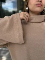 Polerón de cuello alto, color beige, con diseño holgado y mangas amplias con aberturas laterales en el ruedo.