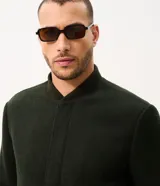 Campera bomber de hombre color verde oscuro, confeccionada en tejido polyvelour de textura aterciopelada. Presenta cuello, puños y cintura elastizados en ribana, cierre frontal oculto y bolsillos laterales.