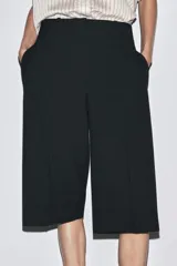 Bermuda larga color marrón oscuro, de tiro medio con cintura con trabillas. Presenta bolsillos laterales ocultos en la costura y detalle de raya planchada. Cierre frontal con cremallera, botón y ganchos metálicos.