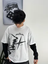 Remera blanca de manga larga con diseño gráfico negro y la inscripción "The Archive" en el frente.