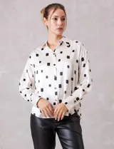 Camisa de satén con estampado de rectángulos negros sobre fondo blanco. Presenta cuello clásico con solapa, cierre frontal con botones metálicos y mangas largas con puños rectos.