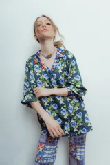 Camisa de seda con estampado de flores azules y verdes sobre fondo oscuro, con cuello camisero y cierre frontal con botones.