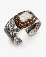 Pulsera tipo brazalete rígido con textura de piel de reptil en tonos grises y blancos. Presenta un aplique central ovalado decorado con una perla barroca rodeada de cristales y pequeñas perlas blancas.