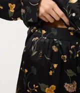 Pijama de dos piezas confeccionado en satén con estampado floral sobre fondo negro. La blusa es estilo camisa con cuello solapa, manga larga y cierre frontal con botones. El pantalón cuenta con cintura elástica y corte recto.