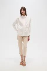 Camisa blanca de algodón, holgada, con cuello camisero, cierre frontal con botones y mangas largas.