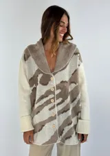 Saco de lana color verde militar con estampado abstracto en tonos verde oliva y detalles bordados en rojo. Tiene cuello solapa, cierre frontal con botones de madera y puños acanalados.