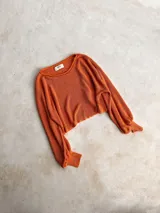 Buzo de tejido de punto color naranja con destellos metalizados, de corte cropped, cuello redondo y mangas largas acampanadas con puños ajustados.