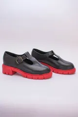 Guillermina de cuero negra con suela tractorada roja y hebilla dorada.