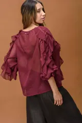 Camisa de estilo romántico color bordó, confeccionada en tela liviana y semitransparente. Presenta volados verticales a lo largo del frente y en las mangas amplias, escote en V y cierre frontal con botones pequeños.