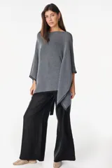 Blusa de punto estilo poncho en color beige, con diseño amplio, cuello redondo y aplique de etiqueta con el logo de la marca en el borde inferior.