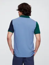 Remera polo de manga corta con diseño color block, cuerpo en azul claro, cuello en verde y mangas en verde y azul marino. Presenta cierre frontal con botones y logo de la marca bordado en el pecho.