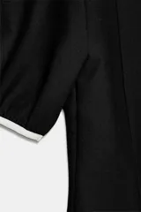 Vestido corto negro con escote en V ribeteado en blanco. Presenta mangas cortas abullonadas y dos lazos blancos decorativos en el centro del pecho.