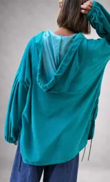 Buzo tipo canguro oversize de tela plush, color azul claro. Presenta capucha, cierre frontal parcial con cordón turquesa y bolsillos canguro frontales. Las mangas son largas y abullonadas con puños ajustados.