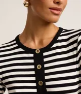 Blusa ajustada de mangas cortas, confeccionada en tejido de punto acanalado con rayas horizontales blancas y negras. Tiene cuello redondo con botones en la vista.