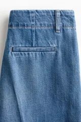 Pantalón de denim de algodón rígido, de corte recto y tiro alto, con pliegues frontales y traseros, bolsillos laterales al bies y cierre oculto.