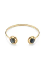 Pulsera rígida abierta de metal dorado, con diseño minimalista y piedras circulares oscuras en los extremos.