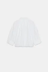 Camisa de algodón con cuello solapa, mangas abullonadas por debajo del codo y bajo acabado en globo. Presenta cierre frontal con botones ocultos.