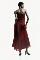 Vestido midi strapless de color bordó, con cuerpo fruncido elástico y falda larga acampanada con un volante en el bajo.