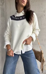 Sweater de punto color natural con cuello redondo y detalle de guarda tejida en la parte superior del pecho. Presenta mangas largas con puños acanalados y un diseño de corte recto.