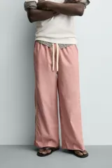 Pantalón de corte relajado confeccionado en popelín de algodón, con estampado de rayas verticales blancas sobre fondo rosado. Posee cintura elástica ajustable con cordón y bandas laterales lisas en color rosado oscuro, ribeteadas con un vivo blanco.
