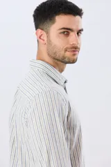 Camisa de manga larga de lino y algodón, con diseño de rayas verticales en tonos celestes y blancos. Presenta cuello camisero, cierre frontal con botones y pequeño bordado al tono en el pecho.