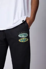 Pantalón jogger de corte oversize confeccionado en tela rústica color verde agua claro. Presenta una estampa gráfica localizada en el muslo izquierdo con diseño de óvalos y estrellas.