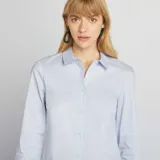 Camisa de corte ajustado en color azul claro, con cuello italiano, cierre frontal de botones y mangas largas con puños abotonados.
