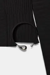 Top corto y ajustado de punto canalé color negro, con cuello redondo, manga larga y detalle de aplique metálico en la parte delantera.