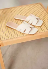 Sandalias planas tipo chinela color camel, con diseño de tiras entrelazadas en forma de "H" y punta cuadrada.