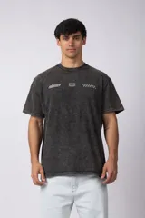 Remera de algodón peinado con efecto desgastado (snow wash), color gris oscuro. Presenta un estampado frontal con texto y un patrón de cuadros de carreras.