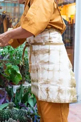 Delantal corto de algodón color crudo con teñido artesanal shibori en tonos marrones.