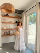 Vestido largo blanco de algodón con tirantes finos, escote en V con detalle de encaje calado y bordado. Falda con múltiples volados y terminaciones con flecos/borlas.