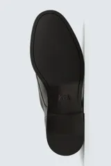 Zapato de vestir estilo monk strap fabricado en piel color marrón oscuro. Presenta ajuste mediante dos hebillas laterales metálicas, detalle de flecos en el empeine y puntera con perforaciones decorativas tipo brogue.