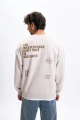 Buzo de corte oversize en color visón, con cuello redondo y puños acanalados. Presenta un diseño estampado en la espalda con tipografía y gráficos en tono marrón.