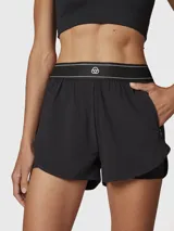 Short deportivo 2 en 1 de color negro, con short interior ajustado y short exterior holgado. Presenta una cintura elástica ancha con detalle de líneas blancas y logo, además de bolsillos laterales invisibles.