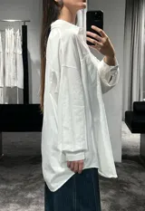 Camisa de corte oversize color marrón, con cuello clásico, cierre frontal de botones y mangas largas con puños ajustables. Presenta un diseño de hombros caídos y un bolsillo frontal en el pecho.