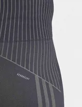 Calza deportiva Adidas Seamless 7/8 de tiro alto, color negro, confeccionada con tejido suave y elástico sin costuras con tecnología AEROREADY. Presenta diseño de líneas acanaladas en la cintura y los tobillos, y las tres tiras características de la marca en el muslo derecho.