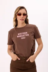Remera de algodón color rosado con cuello redondo y mangas cortas. Presenta un estampado frontal en color negro con el texto 'MIDTOWN MANHATTAN 1997' en tipografía estilo varsity.
