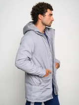 Parka larga gris con capucha, cierre frontal con cremallera y botones a presión, múltiples bolsillos y logo de Umbro en el pecho.