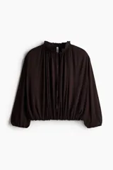 Remera corta oversize de viscosa color marrón, con cuello con volados, abertura frontal con tiras para atar, mangas tres cuartos y elástico fruncido en puños y bajo.