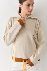 Buzo de punto color beige con rayas verticales marrones, cuello polo con cierre frontal, puños y ruedo acanalados en color marrón. Incluye cordones amarillos ajustables en la cintura.