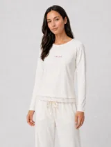 Pijama de algodón color crema, compuesto por una remera de manga larga con bordado delicado en el pecho y un pantalón largo con terminaciones de encaje en el ruedo y la cintura.