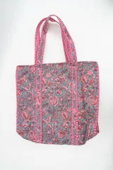 Bolso tipo tote con diseño acolchado, estampado floral en tonos gris y rosado, y detalles de tiras a rayas rojas y blancas en las asas y bordes.