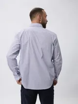 Camisa de manga larga con estampado de microcuadros en tonos azul y blanco. Presenta cuello clásico con botones, cierre frontal abotonado y detalle de logo bordado en el pecho.