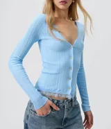 Cardigan de tricot acanalado color beige, de calce ajustado, con mangas largas y escote en V. Cuenta con cierre frontal con botones y detalles de encaje aplicado en el escote y el ruedo.