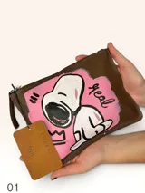 Sobre de cuero marrón con diseño pintado a mano que presenta al personaje Snoopy sobre un fondo rosado y la palabra 'heal'. Cuenta con cierre superior y etiqueta de cuero colgante.
