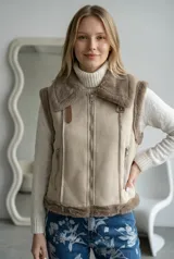 Chaleco estilo gamulán con interior y bordes de piel sintética. Presenta cierre frontal metálico, bolsillos laterales con cierre y detalles de costuras visibles.