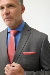 Ambo formal de corte clásico compuesto por saco de dos botones con solapa de muesca y pantalón de vestir a juego, confeccionado en tejido gris de textura fina.