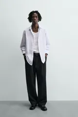 Camisa slim fit blanca con rayas verticales finas en color gris, confeccionada en tejido de algodón. Presenta cuello italiano y manga larga con puño abotonado. Cierre frontal con botonadura.